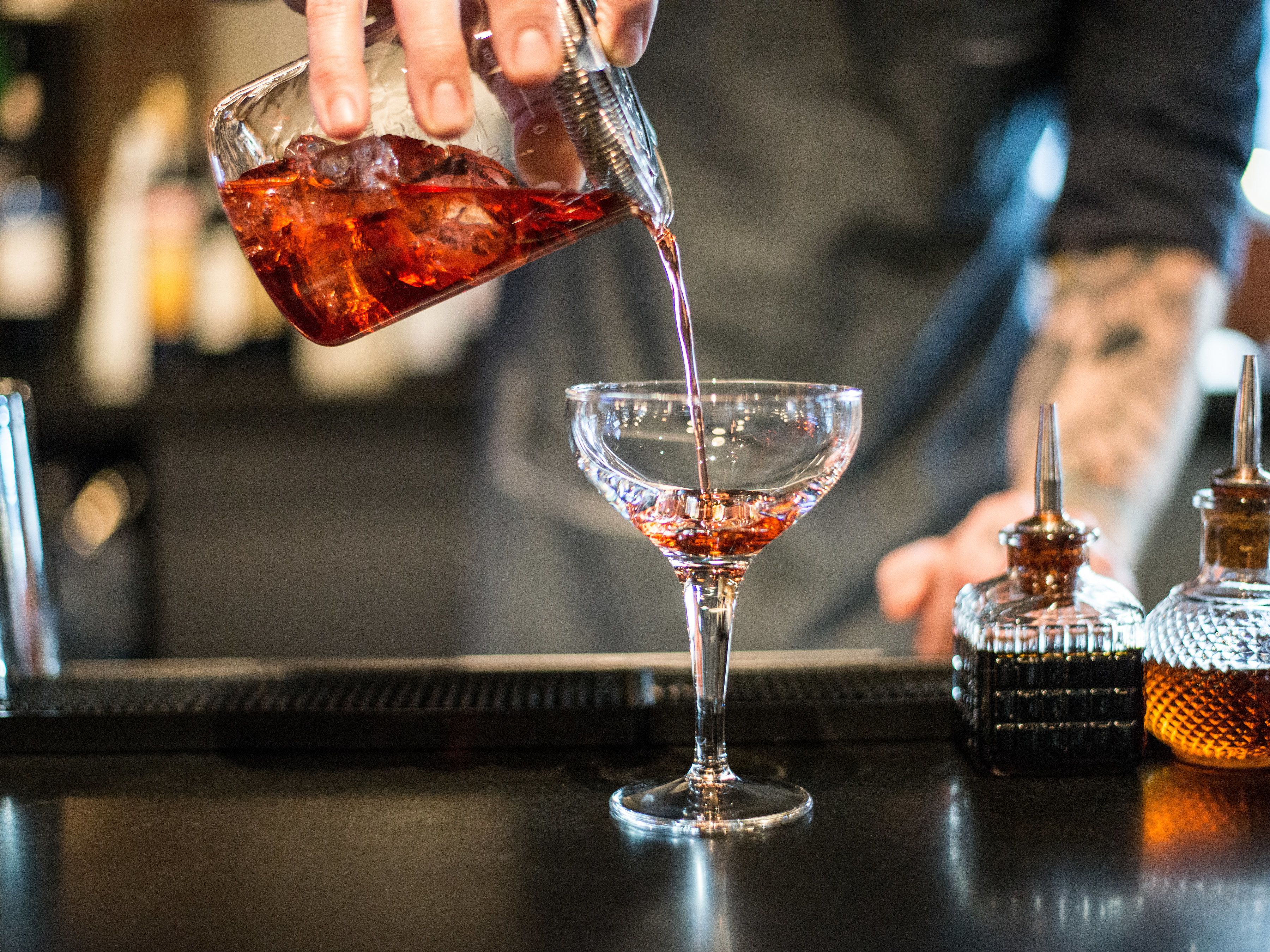 A bartender pouring a drink into a martini glass.