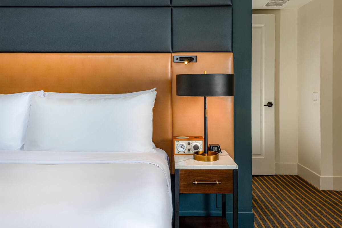 A hotel room with a bed, a nightstand with a lamp, a radio, and a drawer.