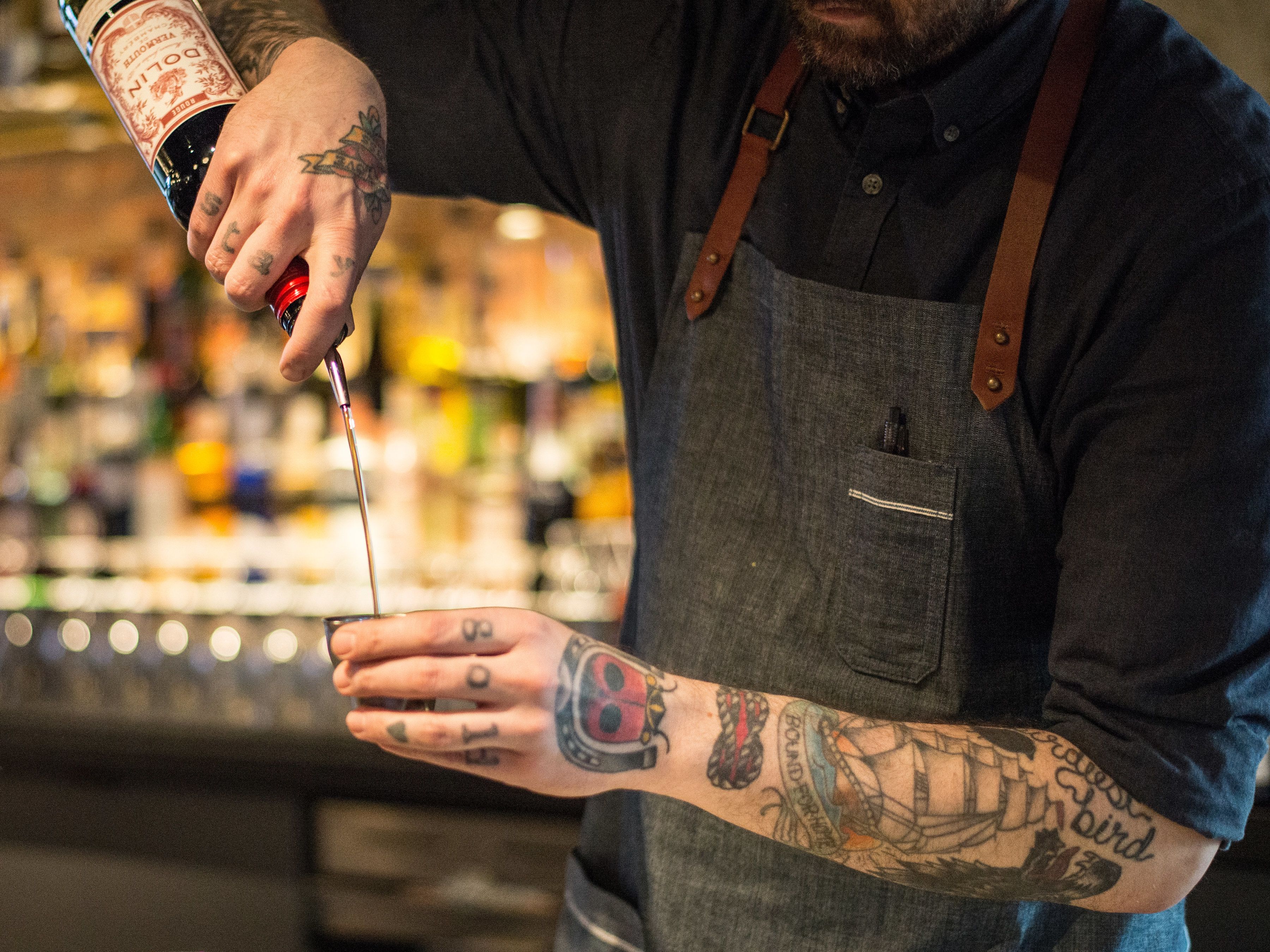 A person with tattoos on their arm holding a bottle with a red cap.
