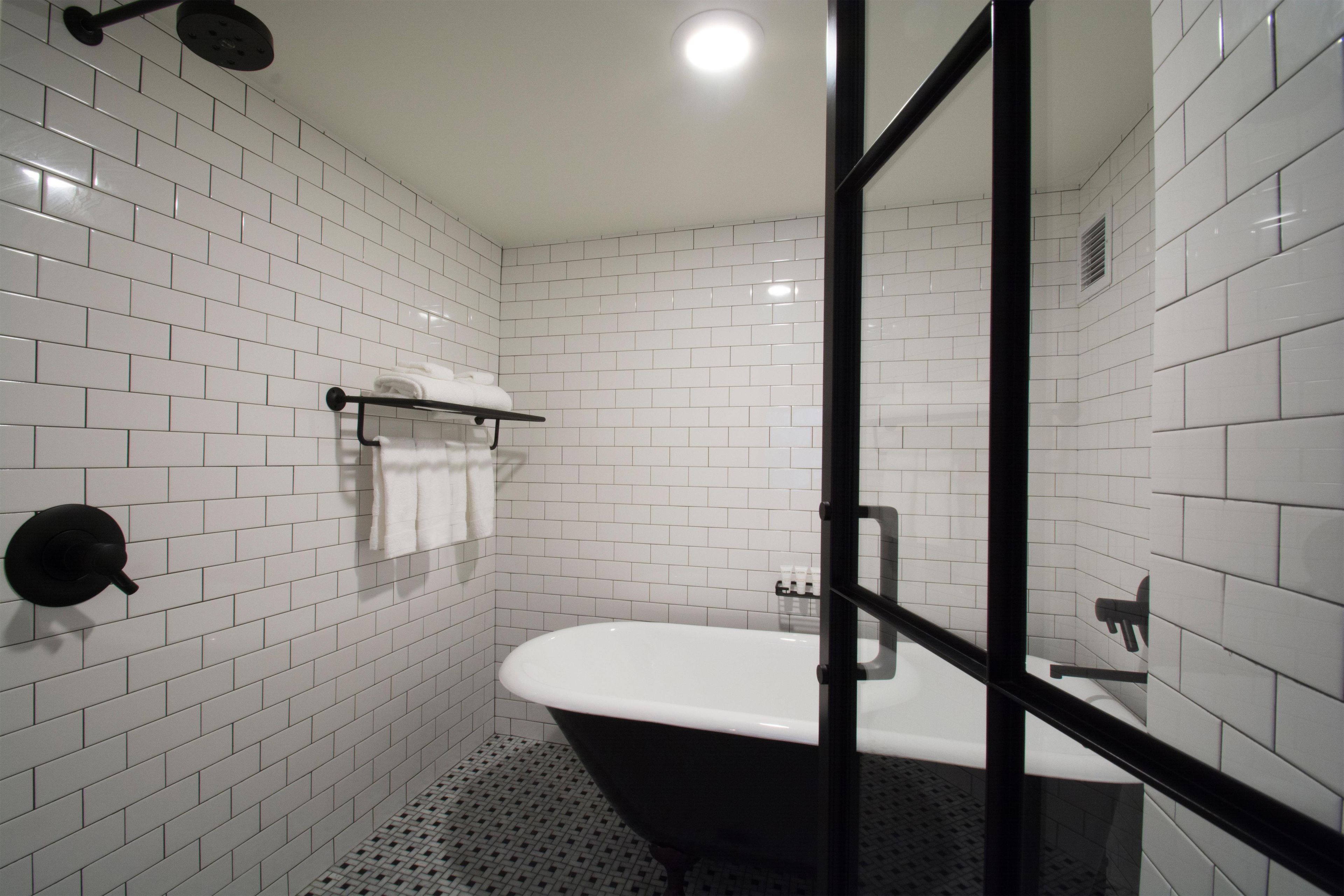 A modern bathroom with white subway tiles, a black bathtub, and a glass shower enclosure.