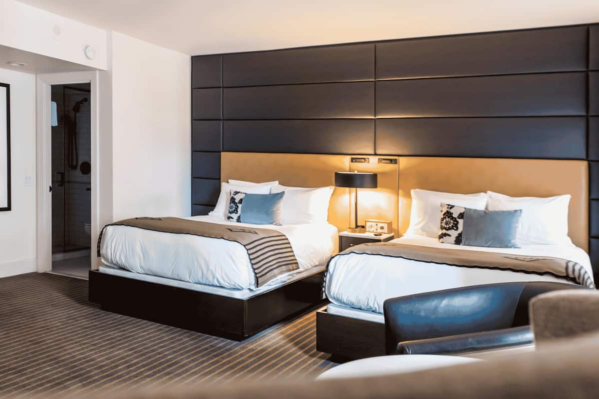 A modern hotel room with a large bed, two bedside tables, a nightstand, and a seating area with a chair.