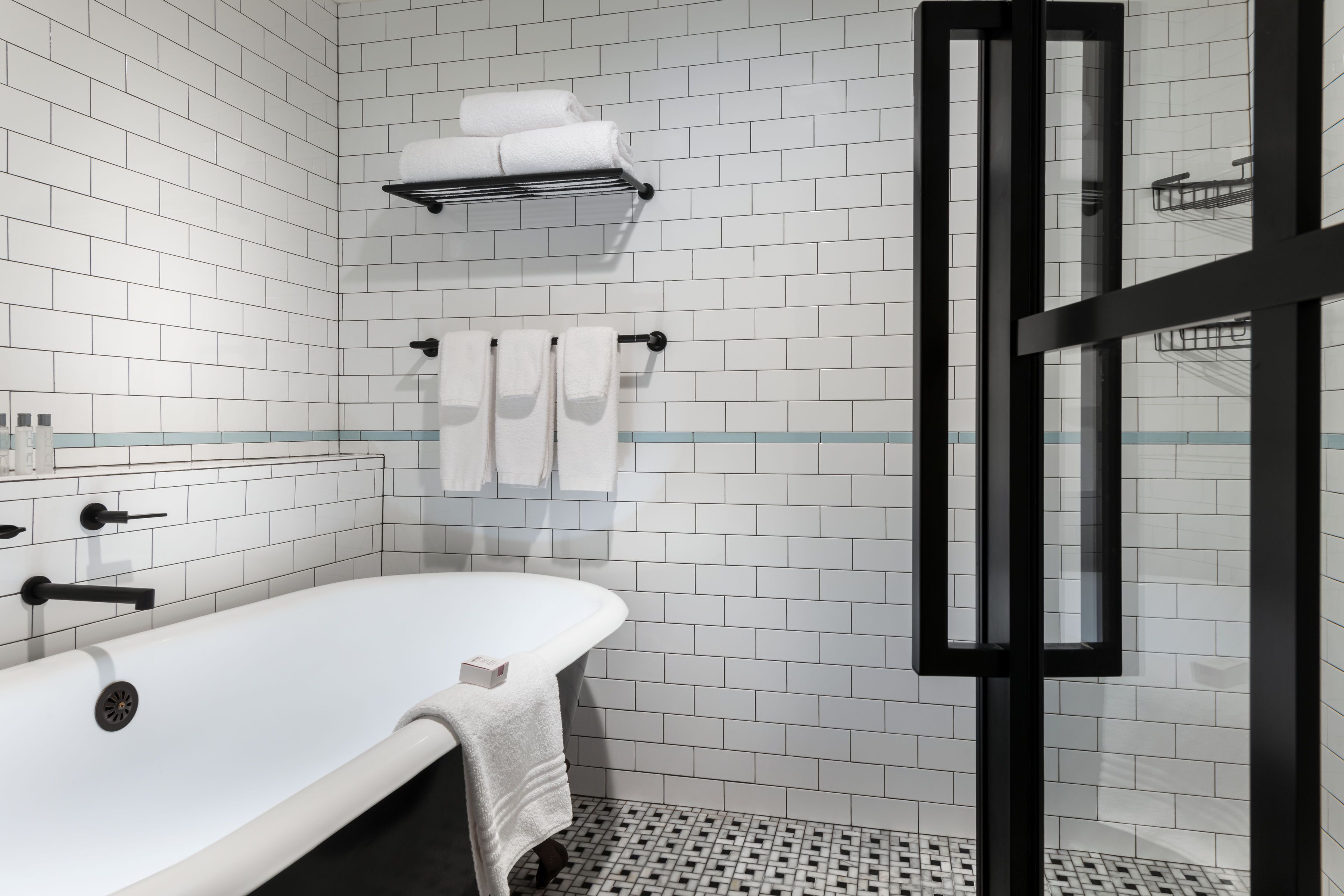 A modern bathroom with white subway tiles, a white bathtub, a glass shower enclosure, and a towel rack with towels.