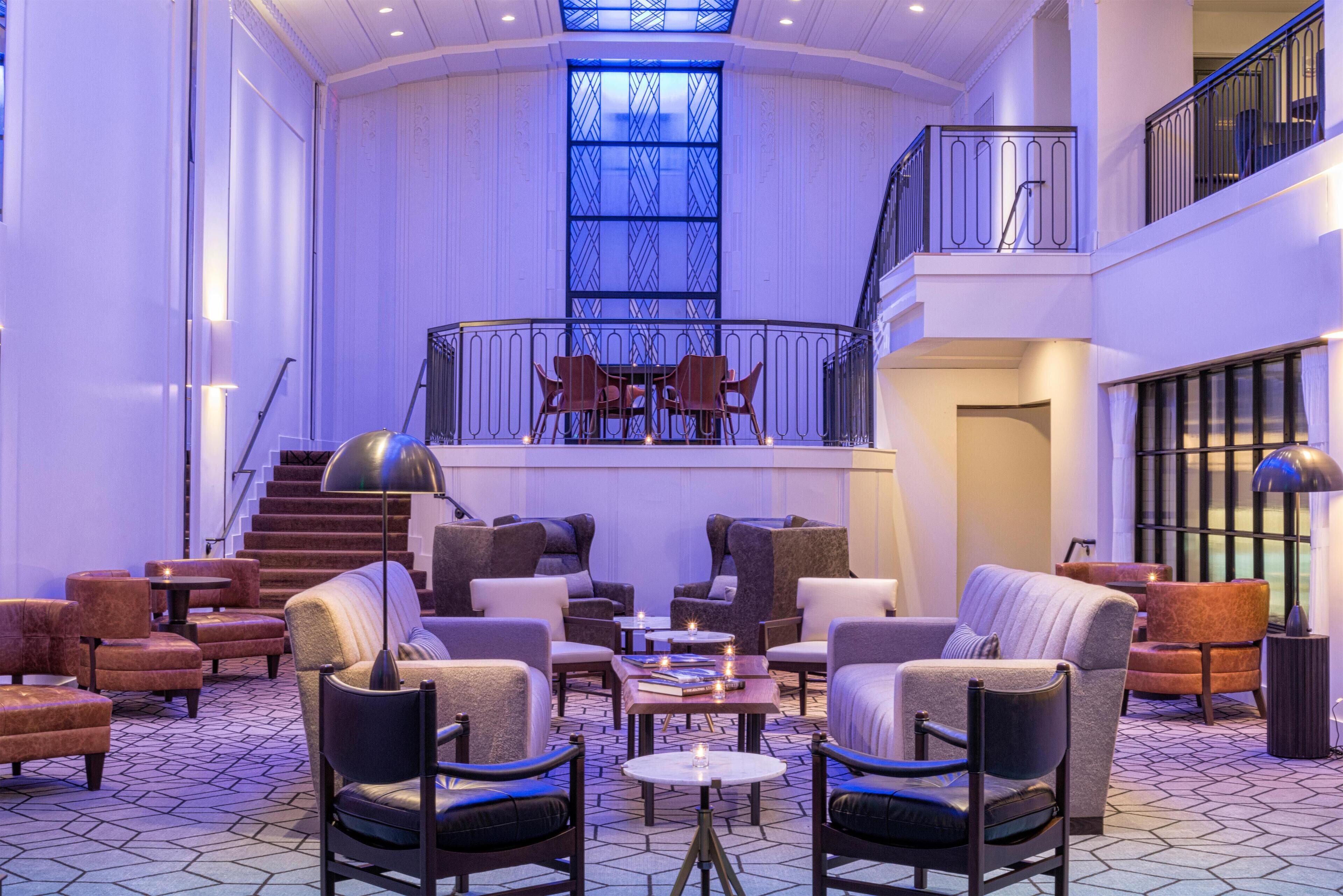 A spacious lobby with a high ceiling, a staircase, and a balcony with seating.