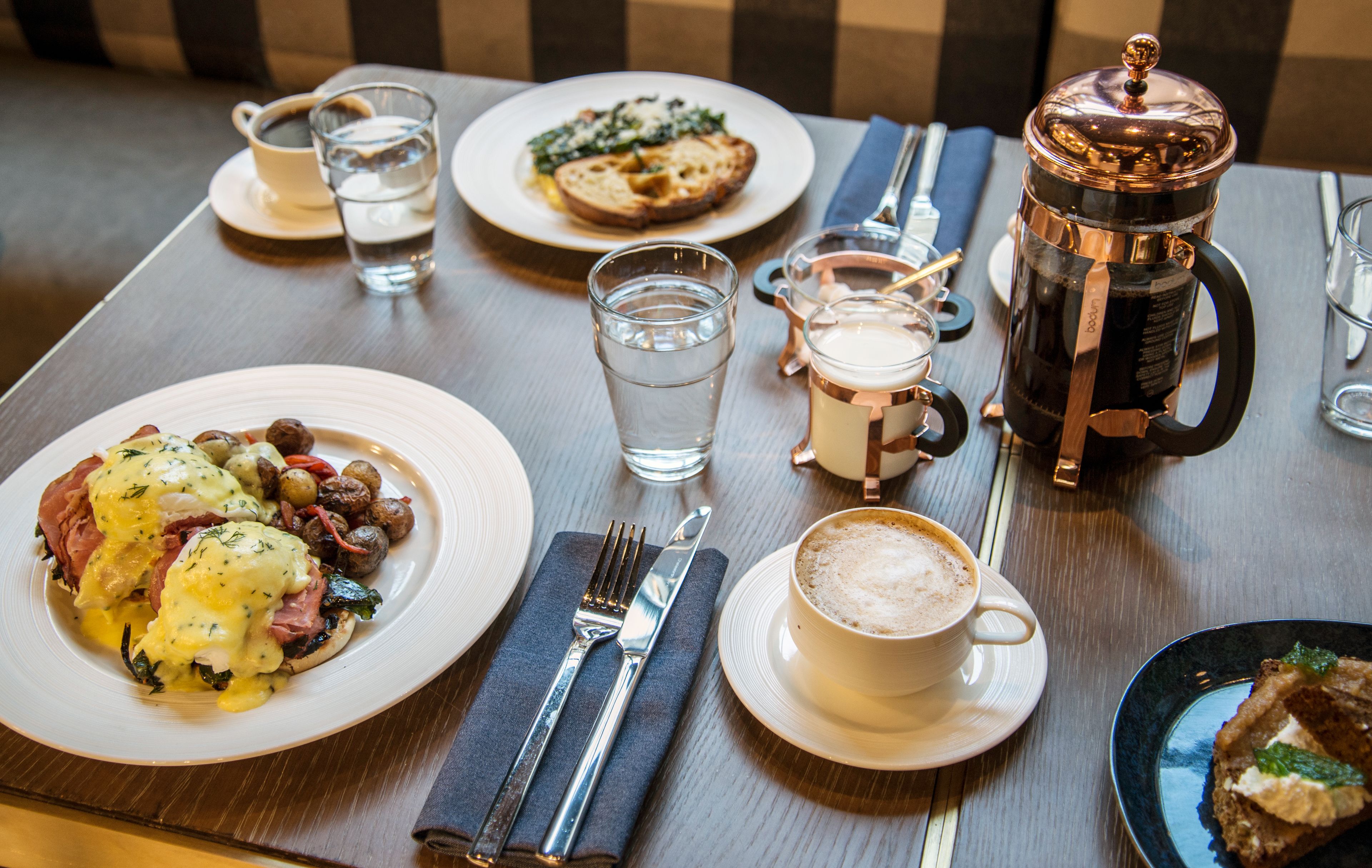 A breakfast setting with plates of food, a coffee pot, and a cup of coffee.