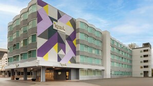 A multi-story hotel with a distinctive geometric facade and a prominent 'spark' logo. - Spark by Hilton Seattle Airport (SeaTac)