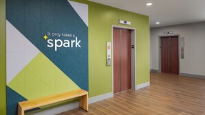 A modern lobby with a geometric wall design, a wooden bench, and an elevator. - Spark by Hilton Seattle Airport (SeaTac)