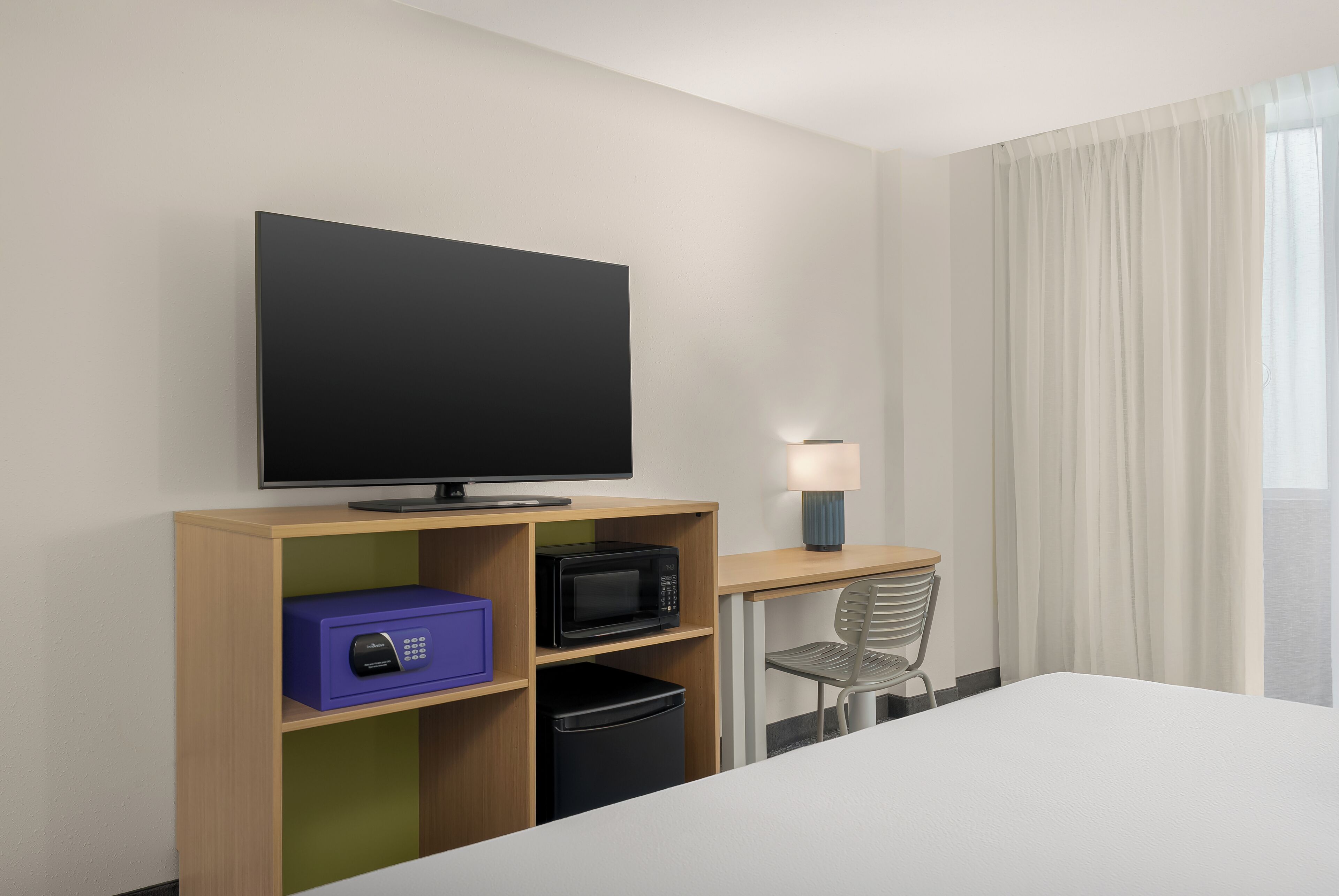 Habitació d'hotel amb llit, televisió, microones, nevera petita, làmpada i cadira.
