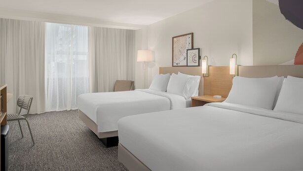 A hotel room with two beds, a desk, a chair, a lamp, and artwork on the wall. - Spark by Hilton Seattle Airport (SeaTac)
