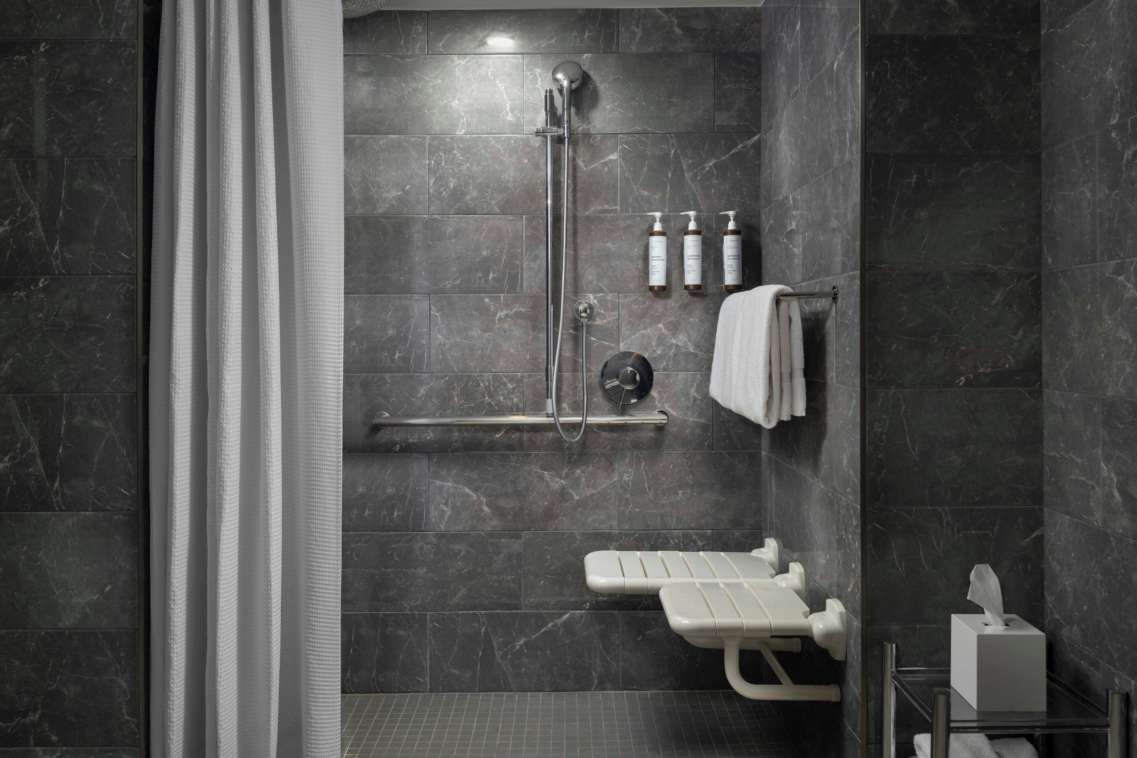 A modern bathroom with a walk-in shower, a bench, and a towel rack.