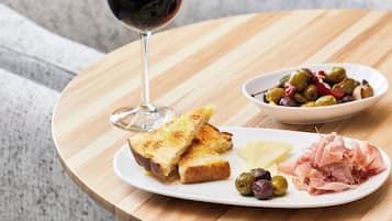 Una mesa de madera con una tostada, aceitunas y jamón, además de una copa de vino tinto.