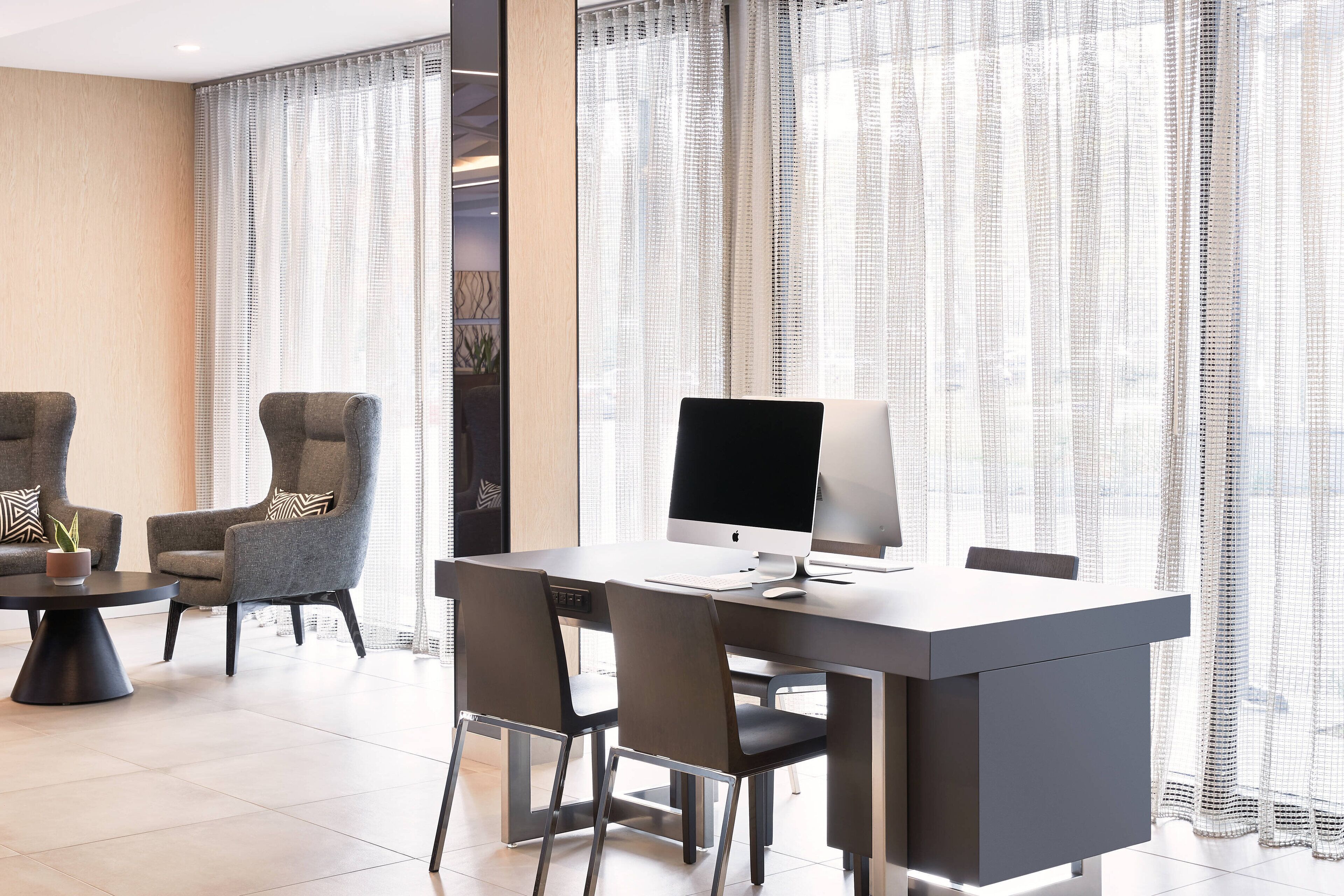 Un espacio de oficina moderno con un escritorio, dos sillones y una mesa redonda.