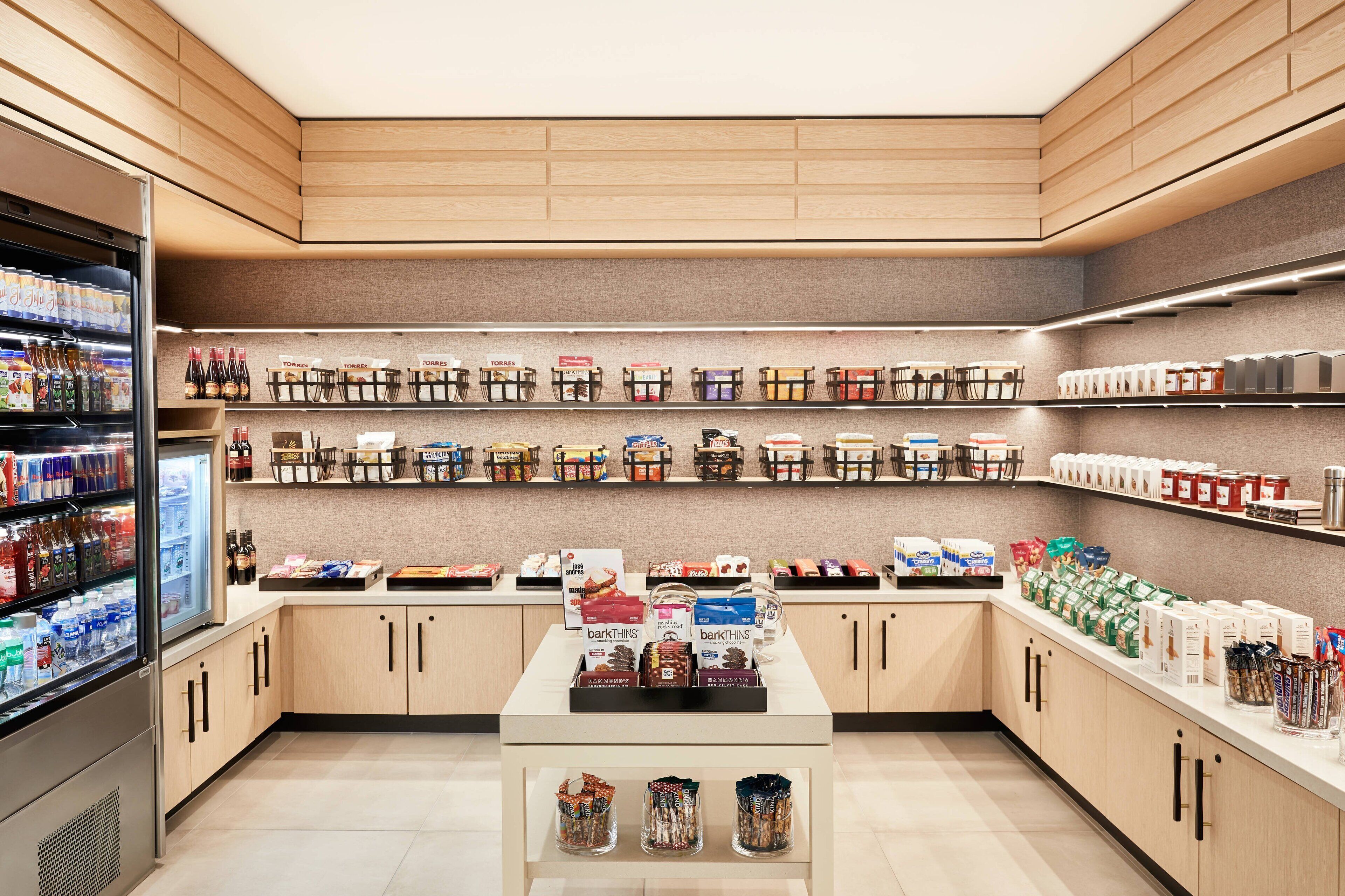 Uma loja bem organizada, com prateleiras repletas de diversos produtos, uma área refrigerada e uma mesa de exposição central.