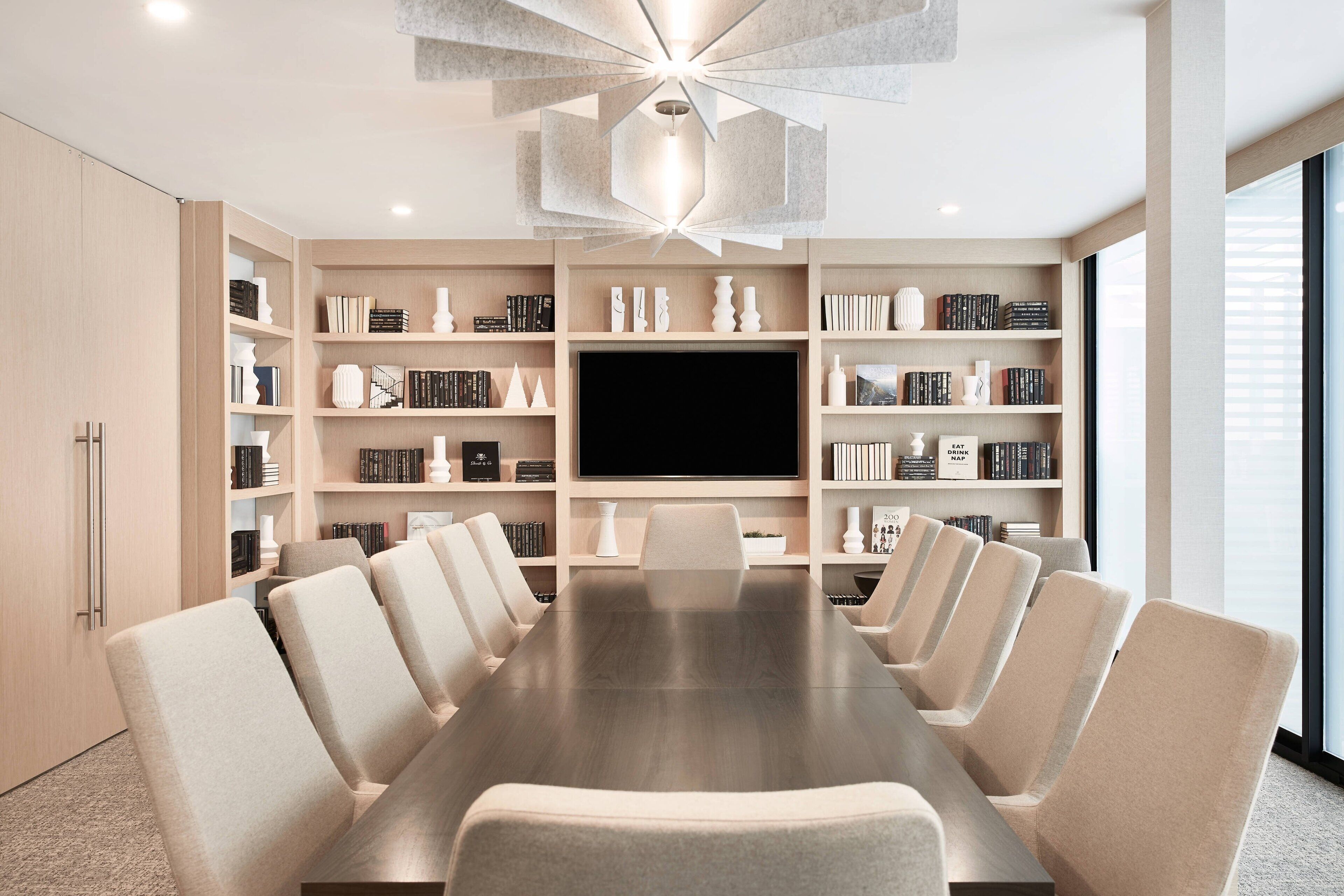 A modern conference room with a long table, multiple chairs, and a large flat-screen TV.