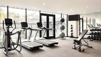 A modern gym with treadmills, elliptical machines, a bench press, and free weights.