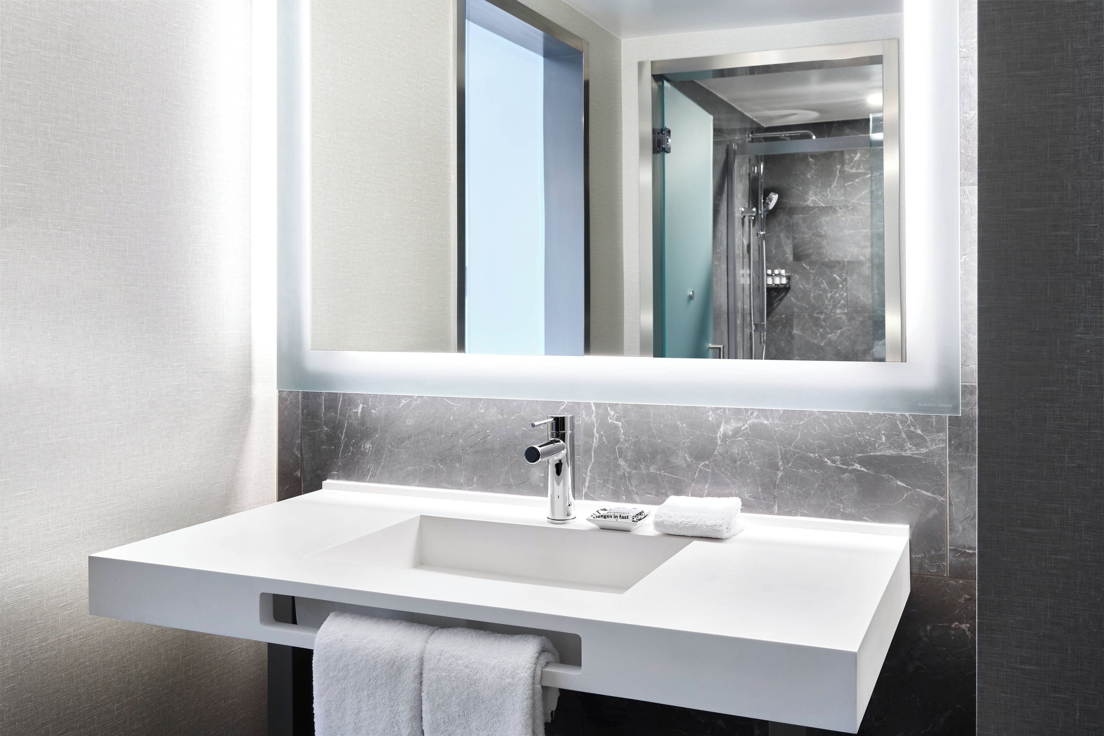 A modern bathroom with a white sink, a mirror, and a shower.