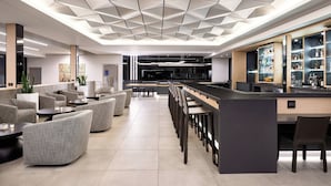 A modern bar area with a geometric ceiling design, bar stools, and a long counter with a glass display case.