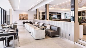 A modern hotel lobby with a seating area, a reception desk, and a bar.