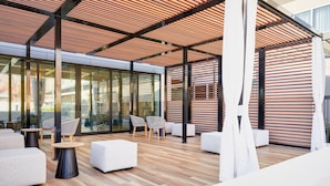An outdoor seating area with modern furniture, a wooden floor, and a glass wall providing a view of the outdoors.