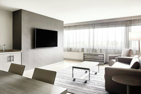 A modern living room with a flat-screen TV mounted on the wall, a dining area with a wooden table and chairs, and a seating area with sofas and a coffee table. - AC Hotel by Marriott Pleasanton (Pleasanton)