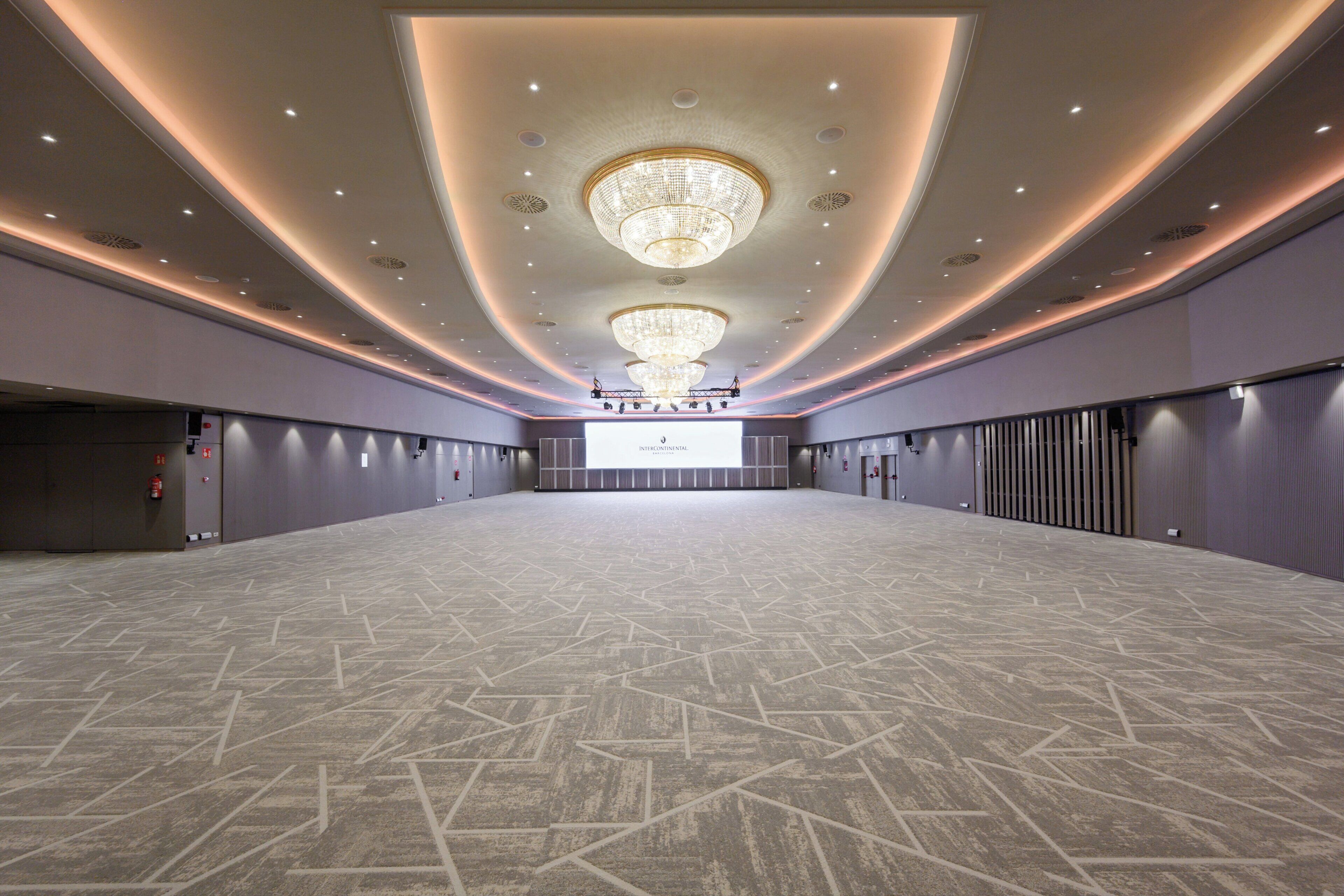 A spacious conference room with a large screen at the front, recessed lighting, and a patterned floor.