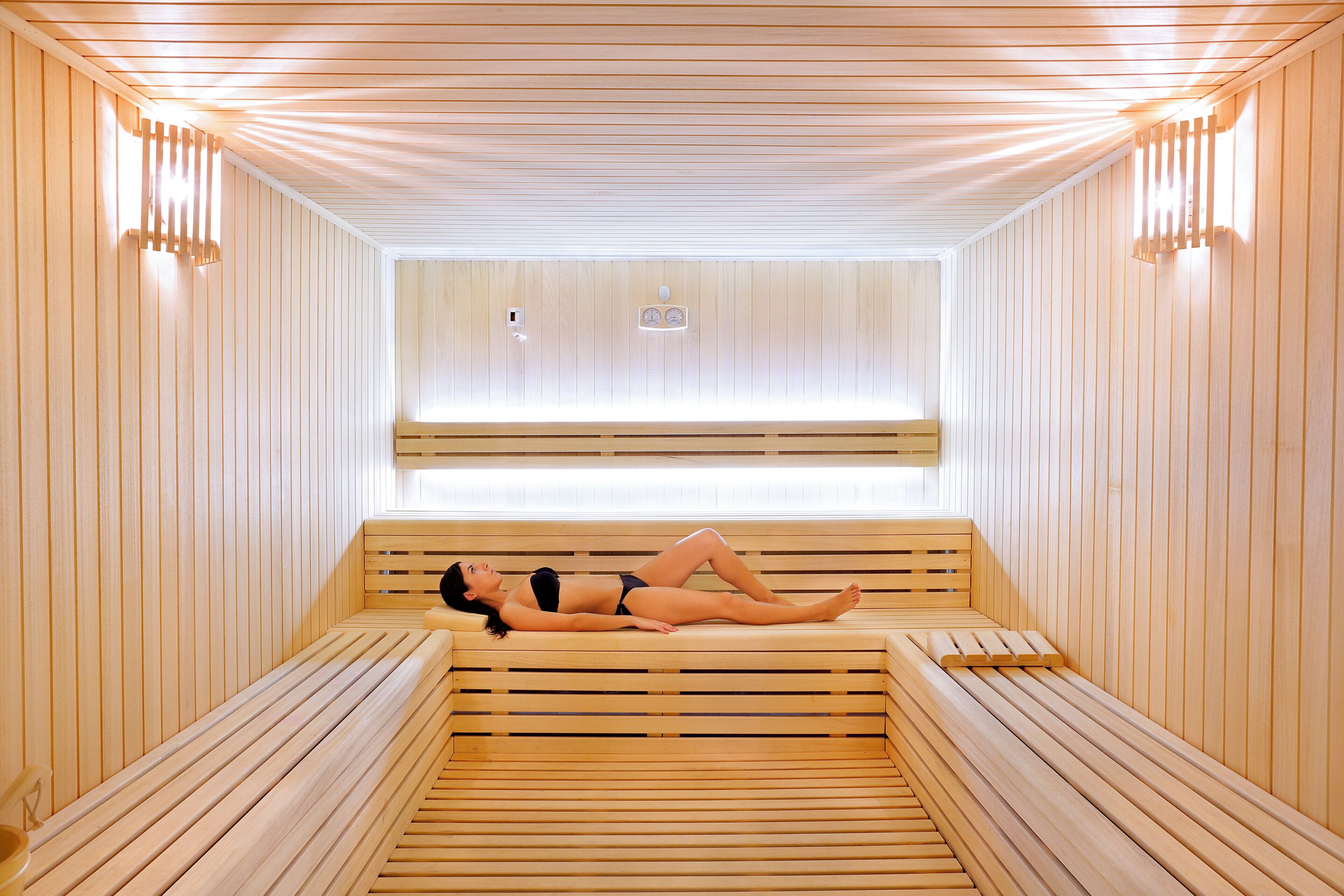 A sauna room with wooden benches and a person lying on one of them.