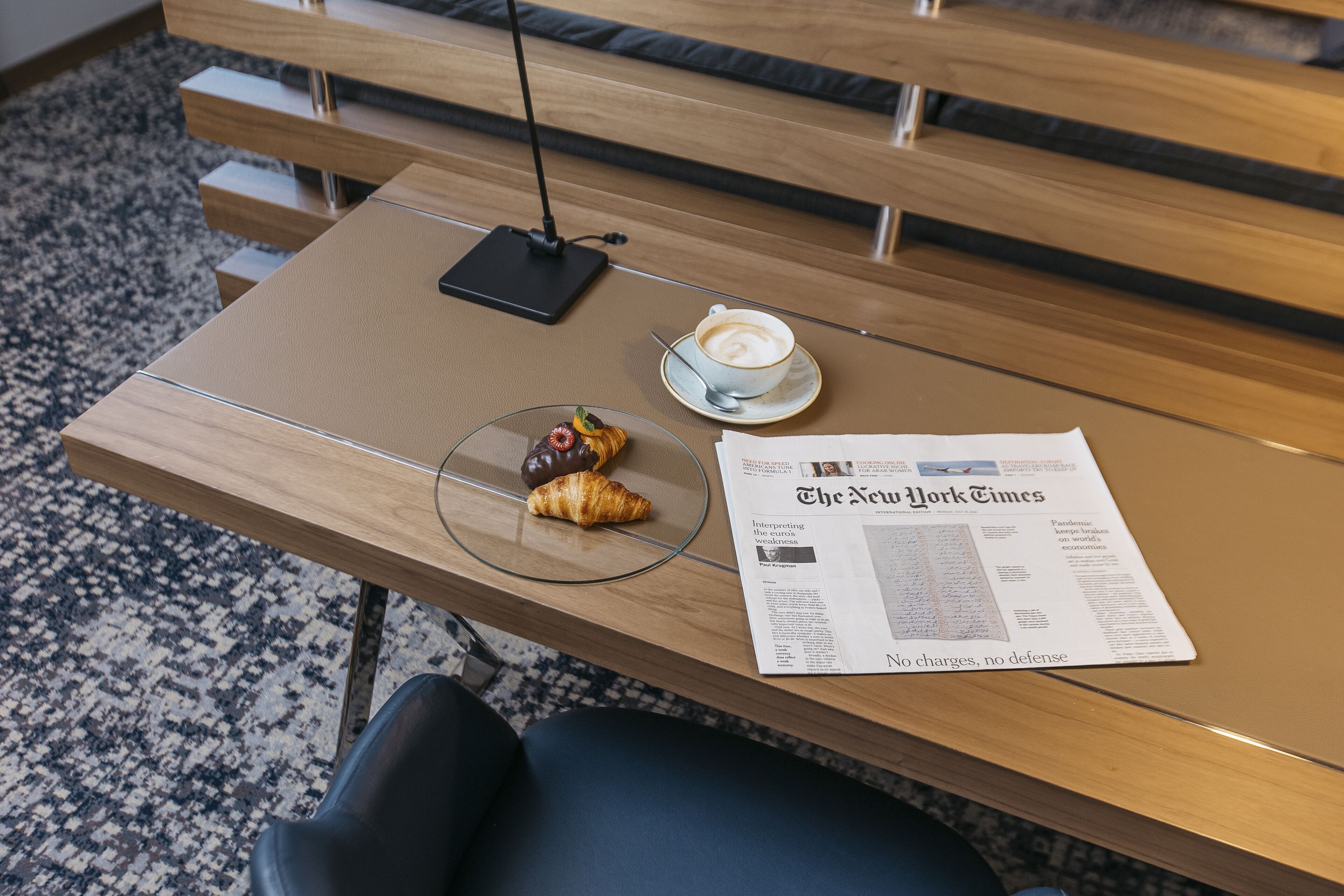 Puisesta pöydästä, jonka päällä on lasilevy, löytyy kannettava tietokone, kahvikuppi, croissant ja sanomalehti.