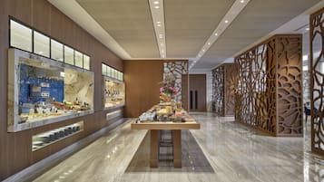 A modern hotel lobby with a marble floor, a buffet area with various food items, and a decorative wooden partition.