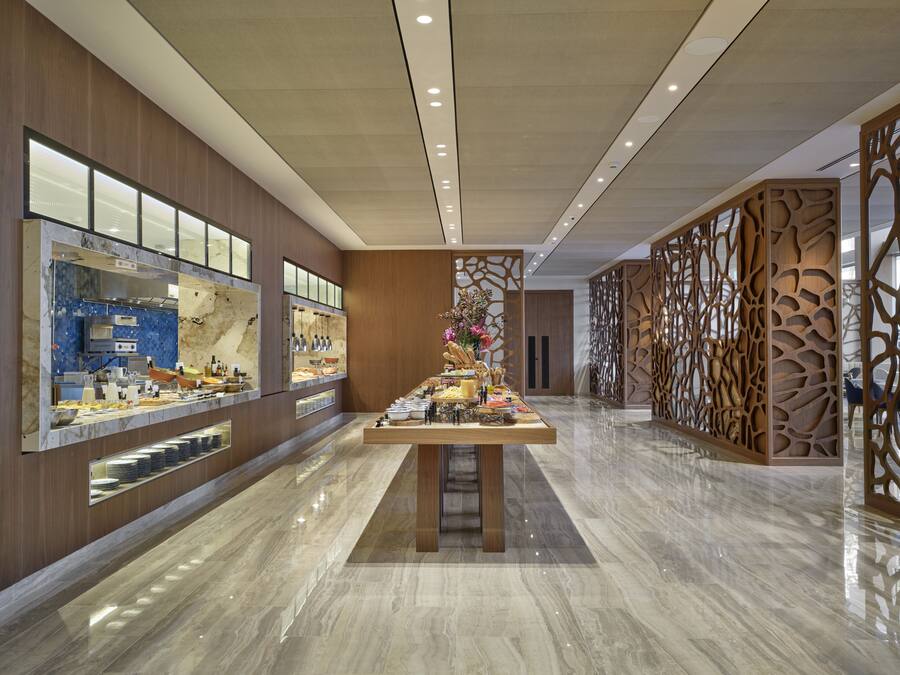 A modern hotel lobby with a marble floor, a buffet area with various food items, and a decorative wooden partition.