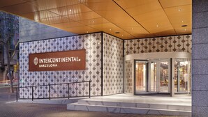 A modern hotel entrance with a geometric patterned facade, a glass revolving door, and a visible outdoor area with a metal railing. - InterContinental Barcelona by IHG (Barcelona)
