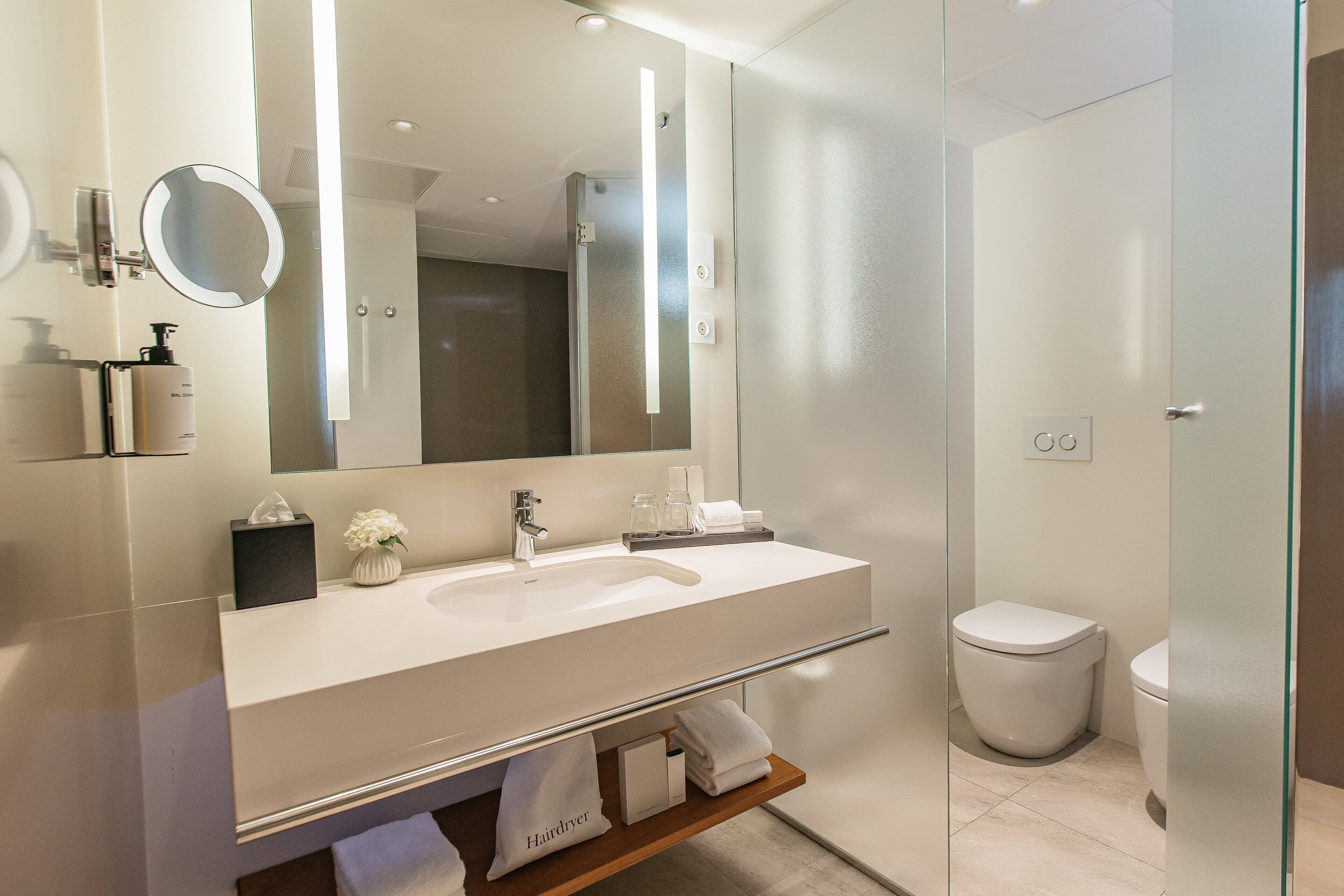 Un baño moderno con un espejo grande, un lavabo blanco y un inodoro.