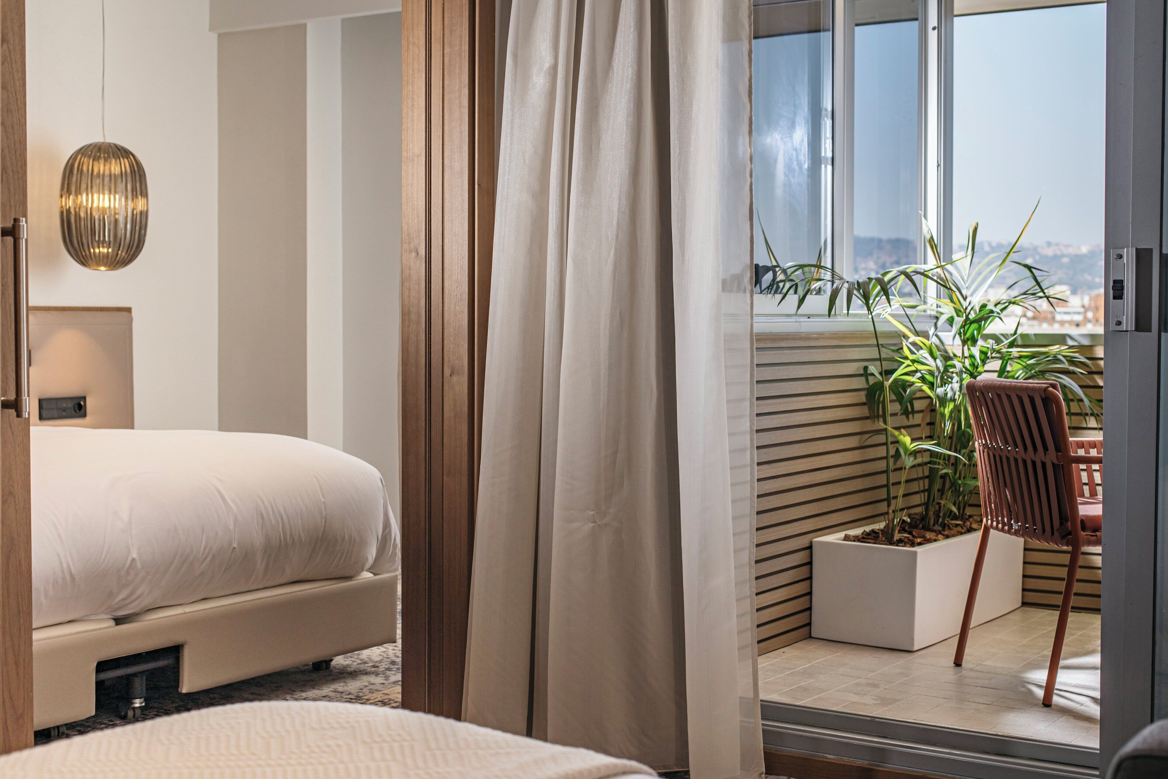 Une chambre moderne avec un grand lit, une vue sur la ville depuis un balcon et une plante en pot.