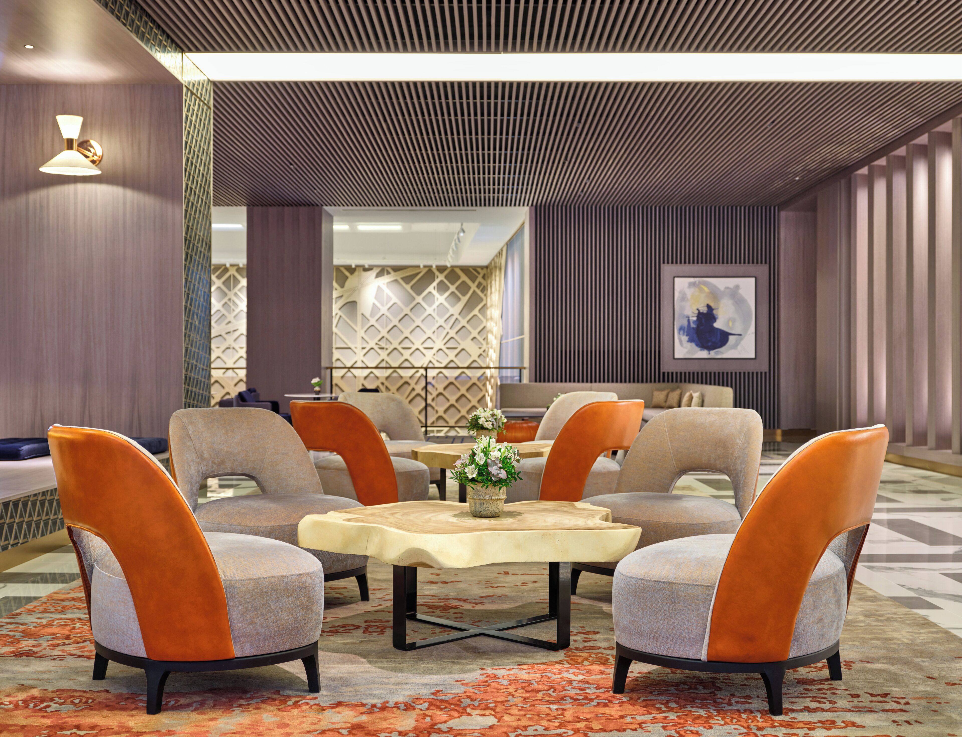 A modern interior with a central seating area featuring four chairs and a table, surrounded by patterned walls and a geometric ceiling design.