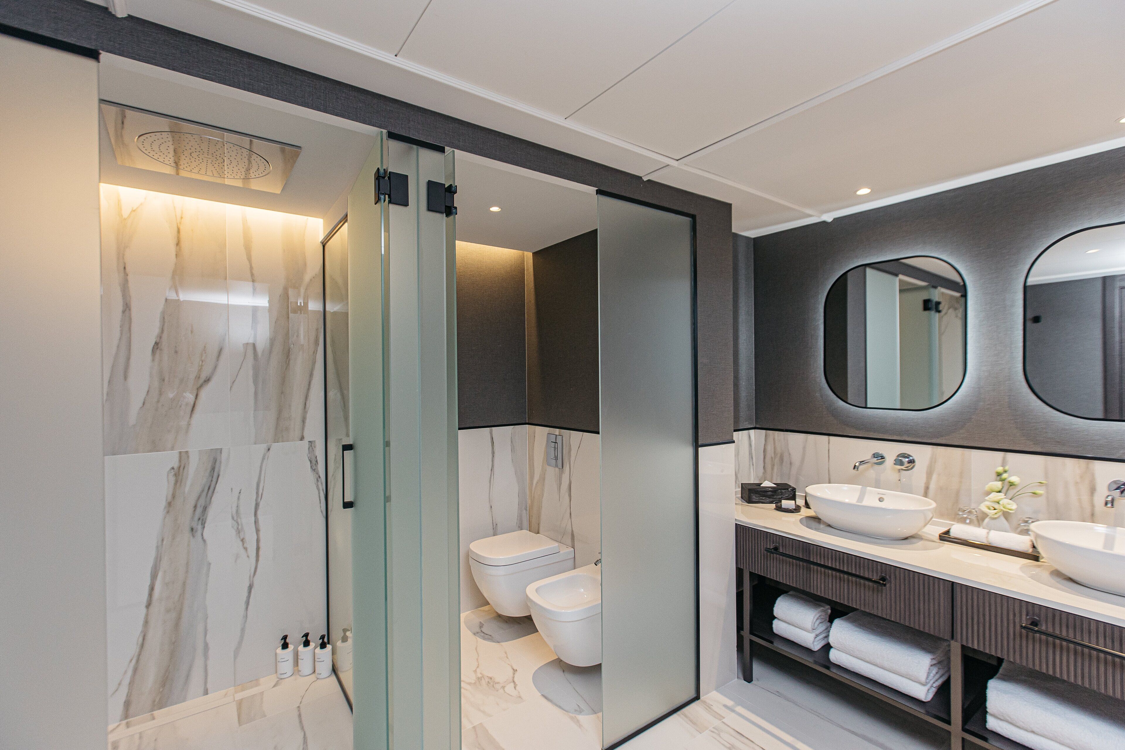 A modern bathroom with a glass-enclosed shower, a double sink vanity, and a large mirror.
