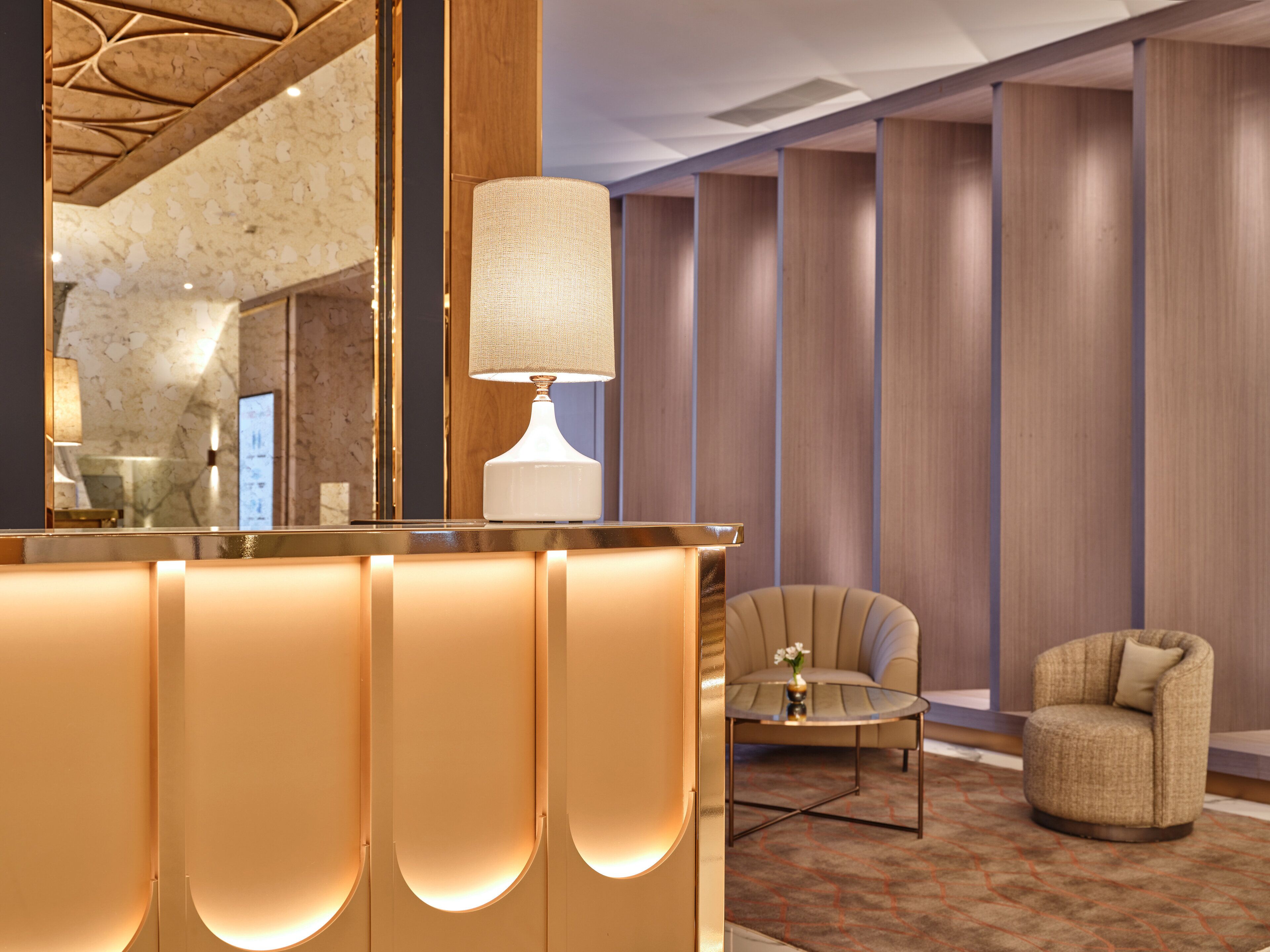 A hotel lobby with a reception desk, a lamp, a sofa, and a chair.