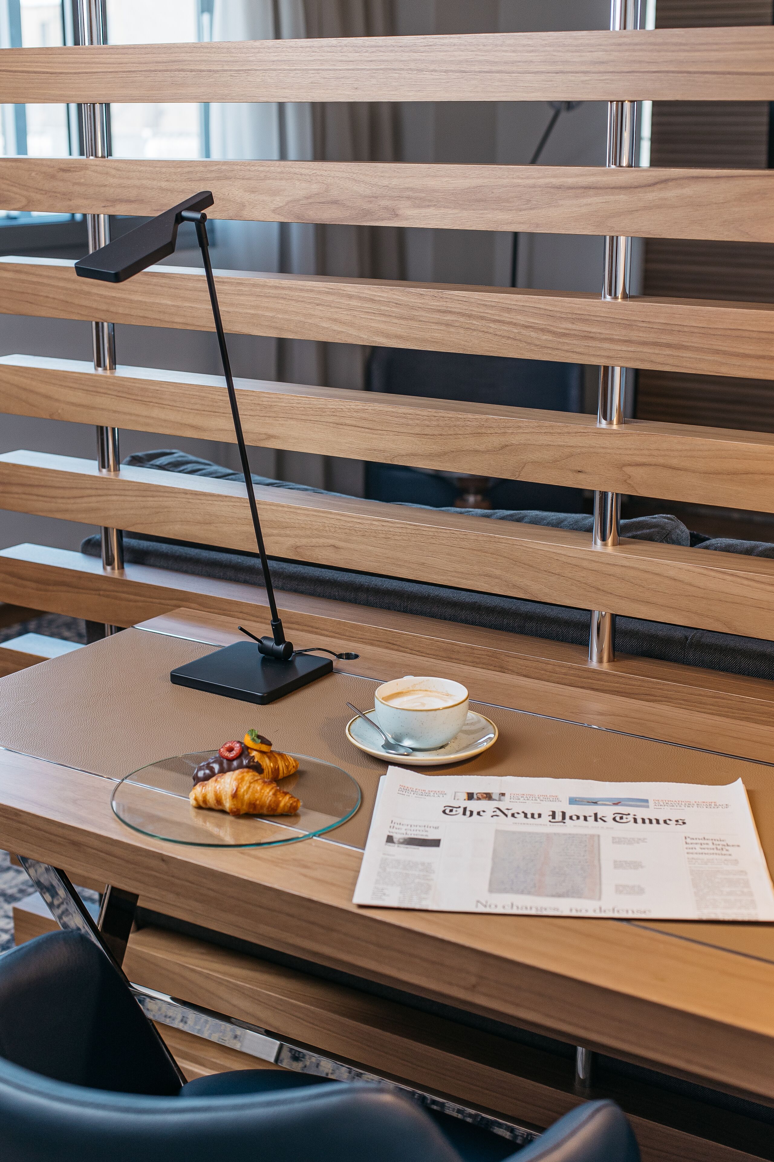 Un banc en bois avec un ordinateur portable, une tasse de café, un croissant et un journal.