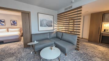 A hotel room with a gray sofa, a small round table, a bed, and a framed picture of a Ferris wheel.
