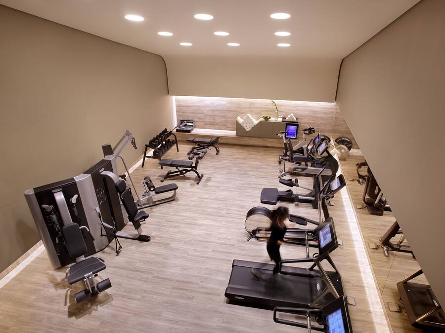 Un gimnasio con diversos equipos de ejercicio, incluyendo cintas de correr y máquinas de pesas, y piso de madera.