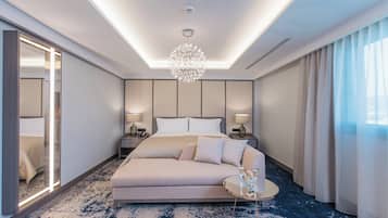 A modern hotel room with a large bed, a sofa, a round coffee table, and a chandelier.
