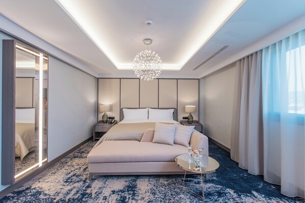 A modern hotel room with a large bed, a sofa, a round coffee table, and a chandelier. - InterContinental Barcelona by IHG (Barcelona)