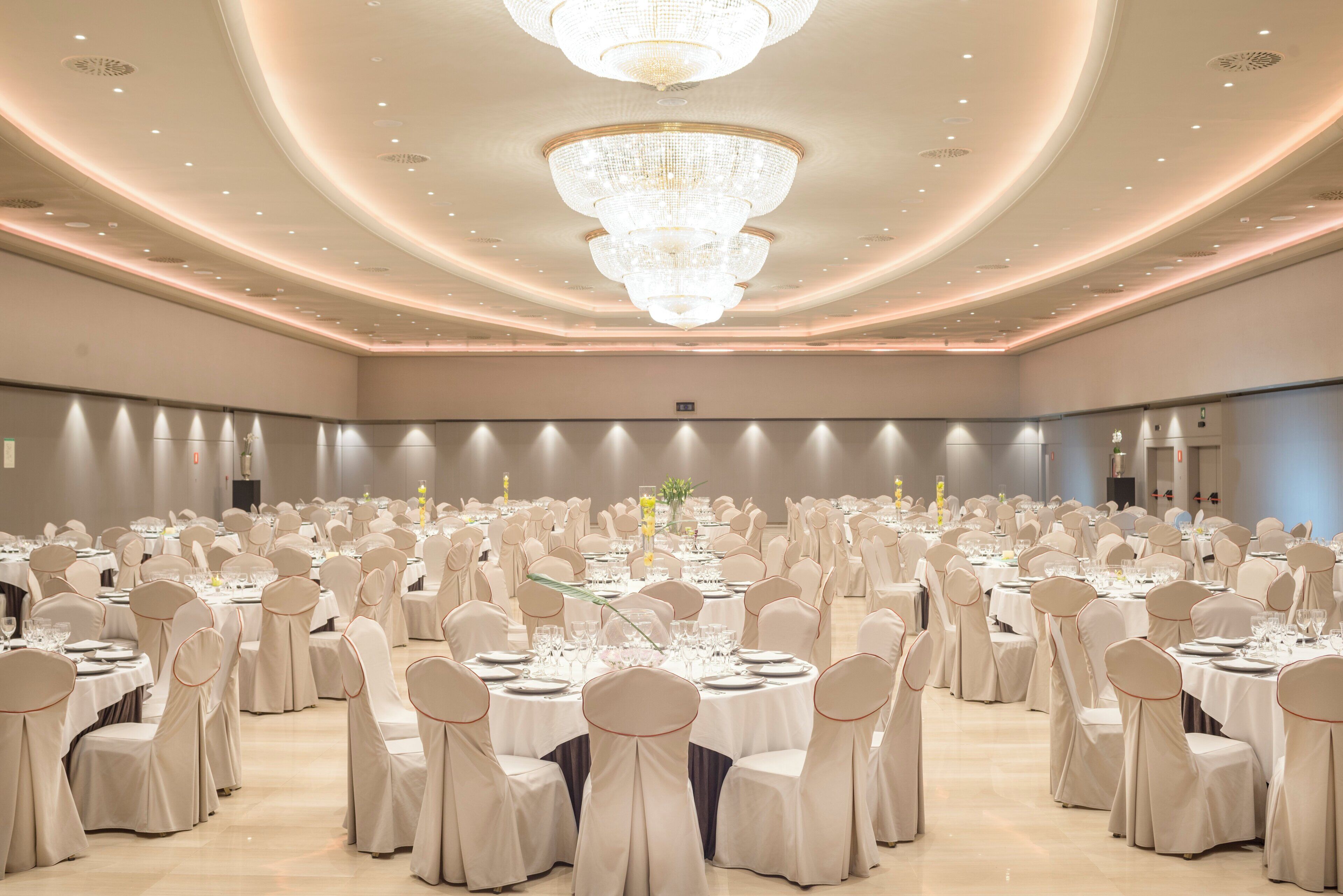 A banquet hall with round tables, chairs, and chandeliers.