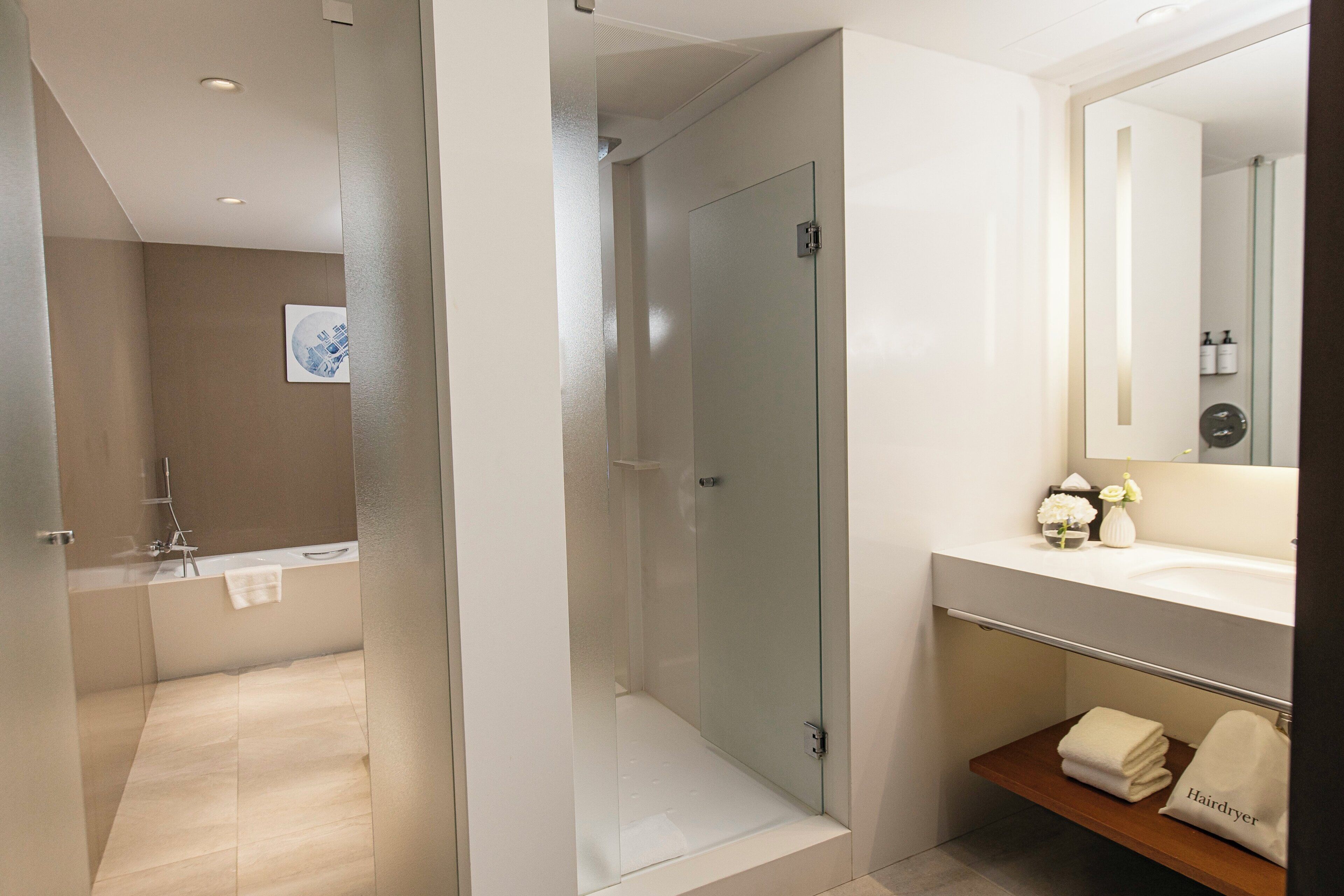 A modern bathroom with a glass shower enclosure, a bathtub, and a vanity with a mirror.