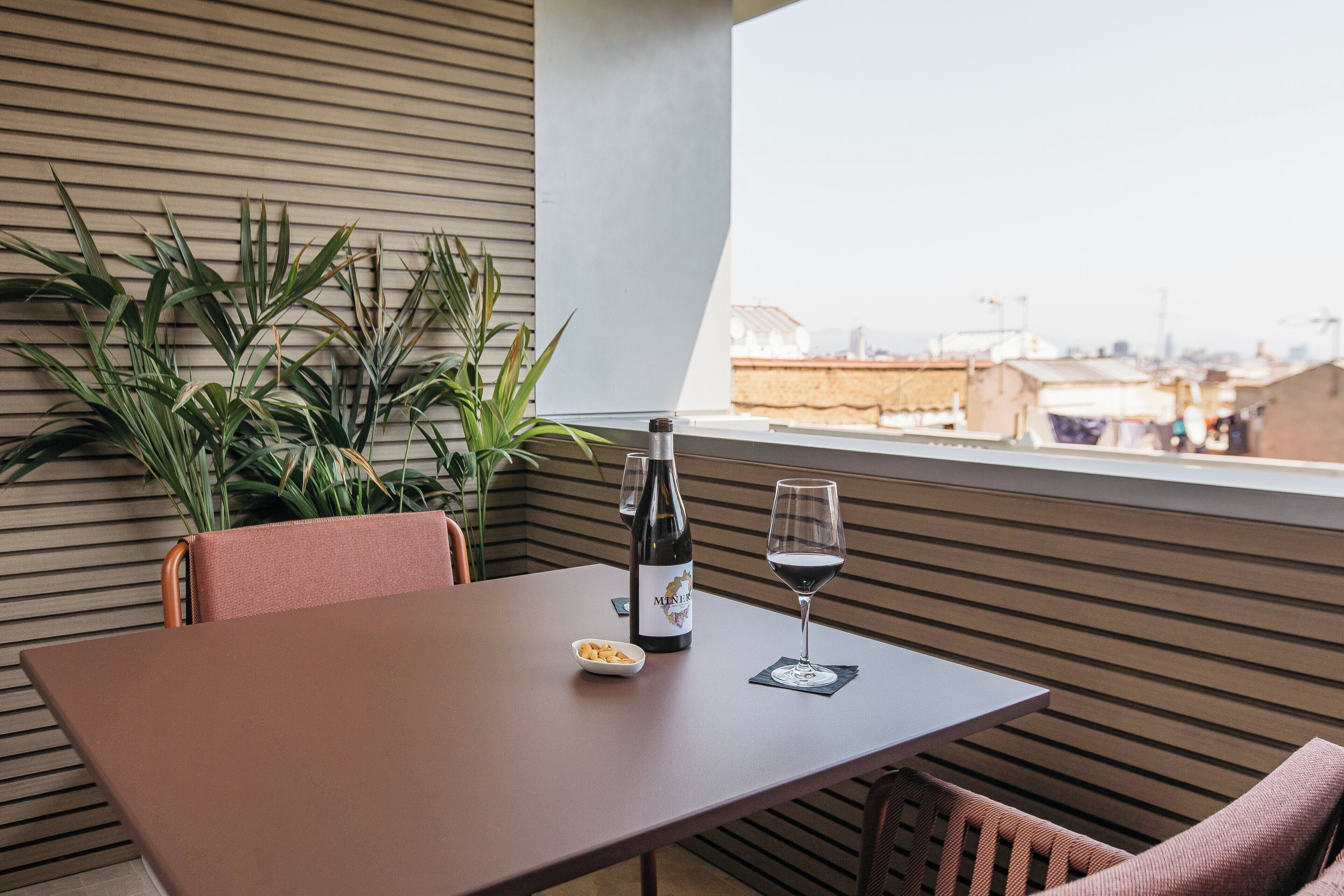 Une table avec une bouteille et un verre, un bol de noix et une plante, le tout dans une pièce moderne avec vue.
