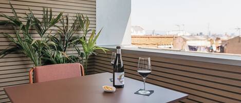 Uma mesa com uma garrafa, um copo, um recipiente com frutos secos e uma planta em um quarto moderno com vista.