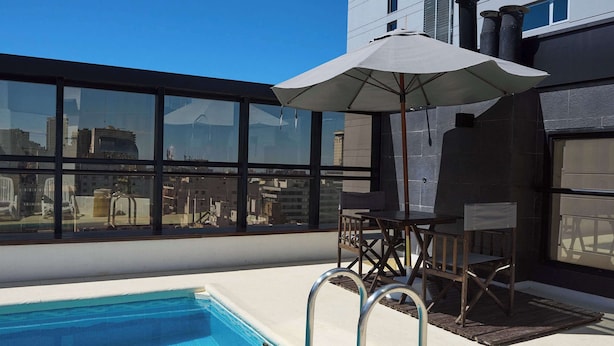 A rooftop pool area with a clear view of the city skyline, a table with chairs, and an umbrella. - Ramada by Wyndham Buenos Aires Centro (Buenos Aires)