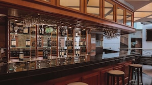 A bar area with a polished black countertop, wooden bar stools, and a variety of bottles and glasses. - Ramada by Wyndham Buenos Aires Centro (Buenos Aires)