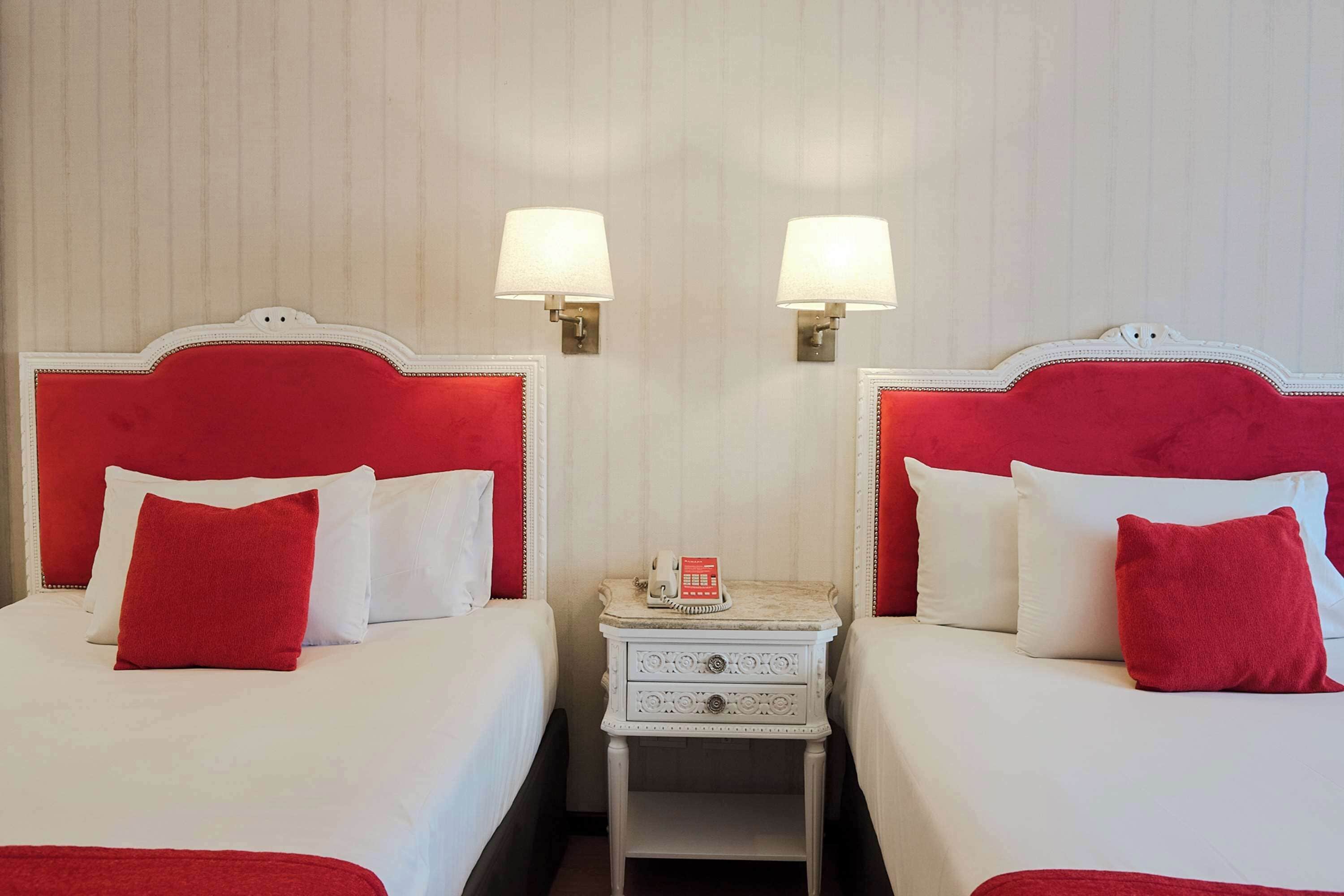 A hotel room with two beds, each with a red headboard and white bedding. There are two bedside tables with lamps and a telephone on one of them.