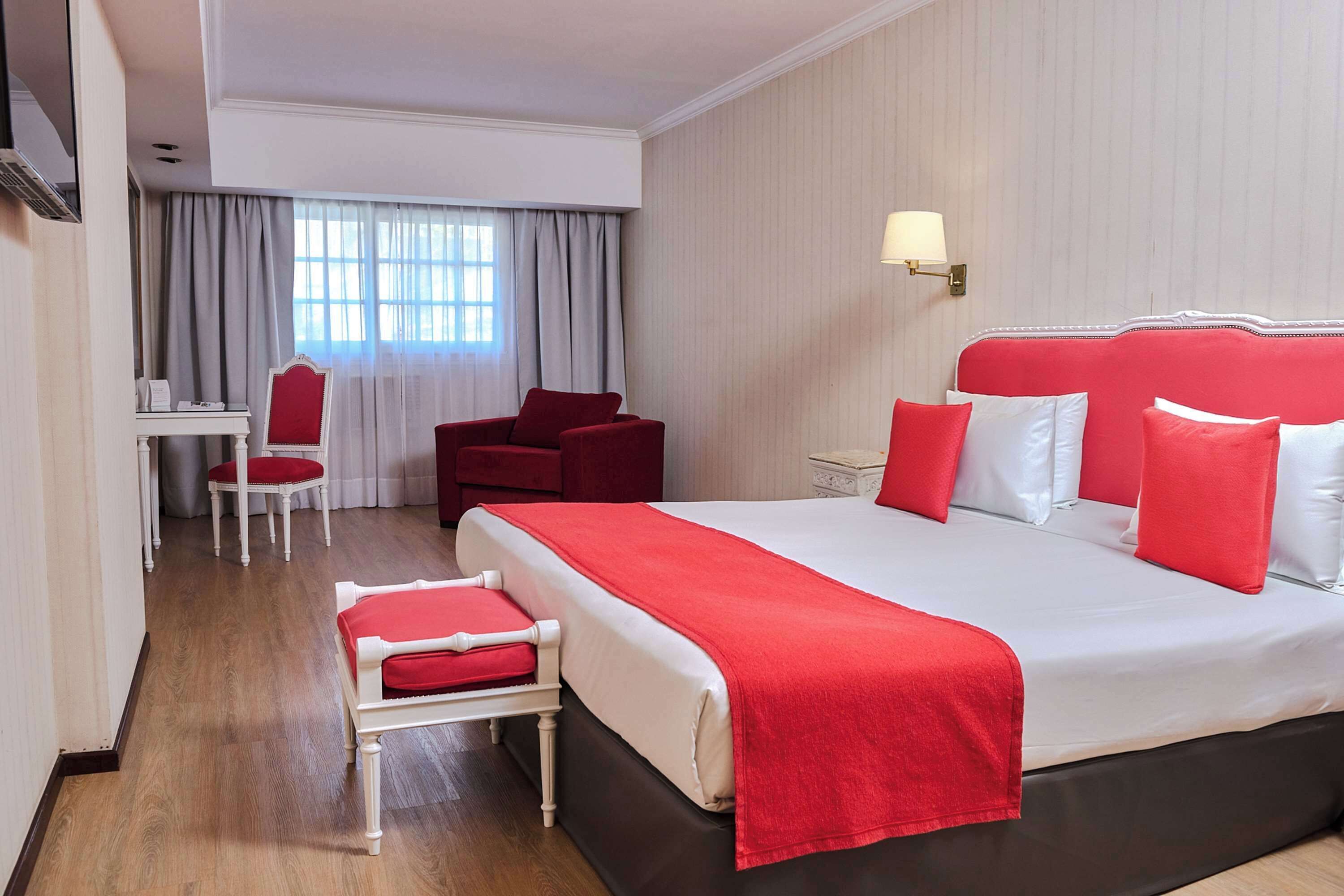 A hotel room with a large bed, a desk, a chair, and a window with curtains.