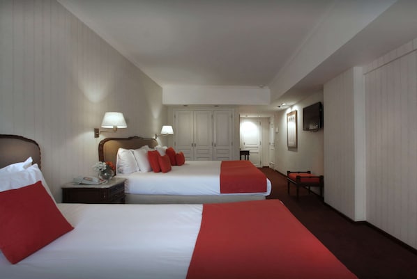 Habitación de hotel con dos camas, un escritorio, una silla, un televisor y una puerta que da a un baño.