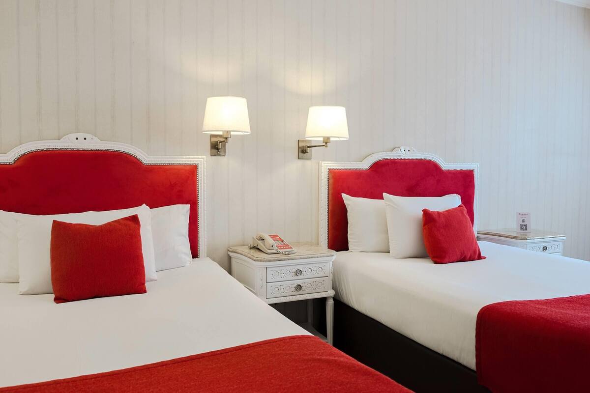 A hotel room with two beds, white bedding, red headboards, bedside lamps, a nightstand with a phone, and a small table with a tray.