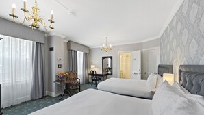 A hotel room with two beds, a desk with a chair, a chandelier, and a large mirror.